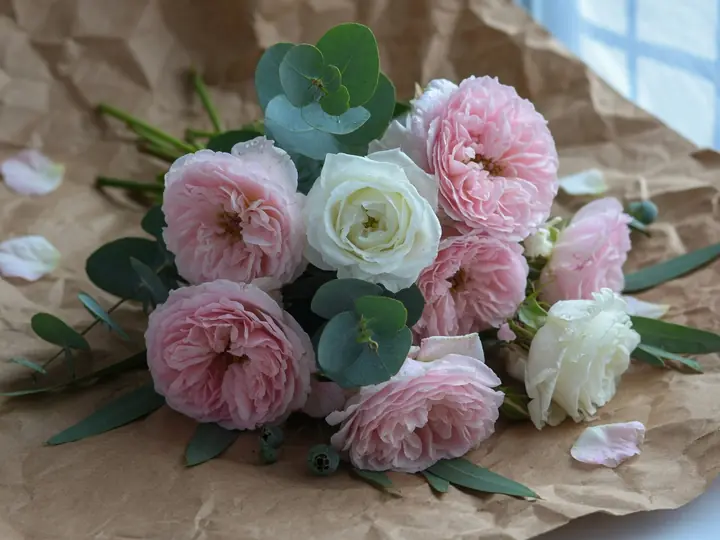 A bouquet of pink roses and white blooms wrapped in paper